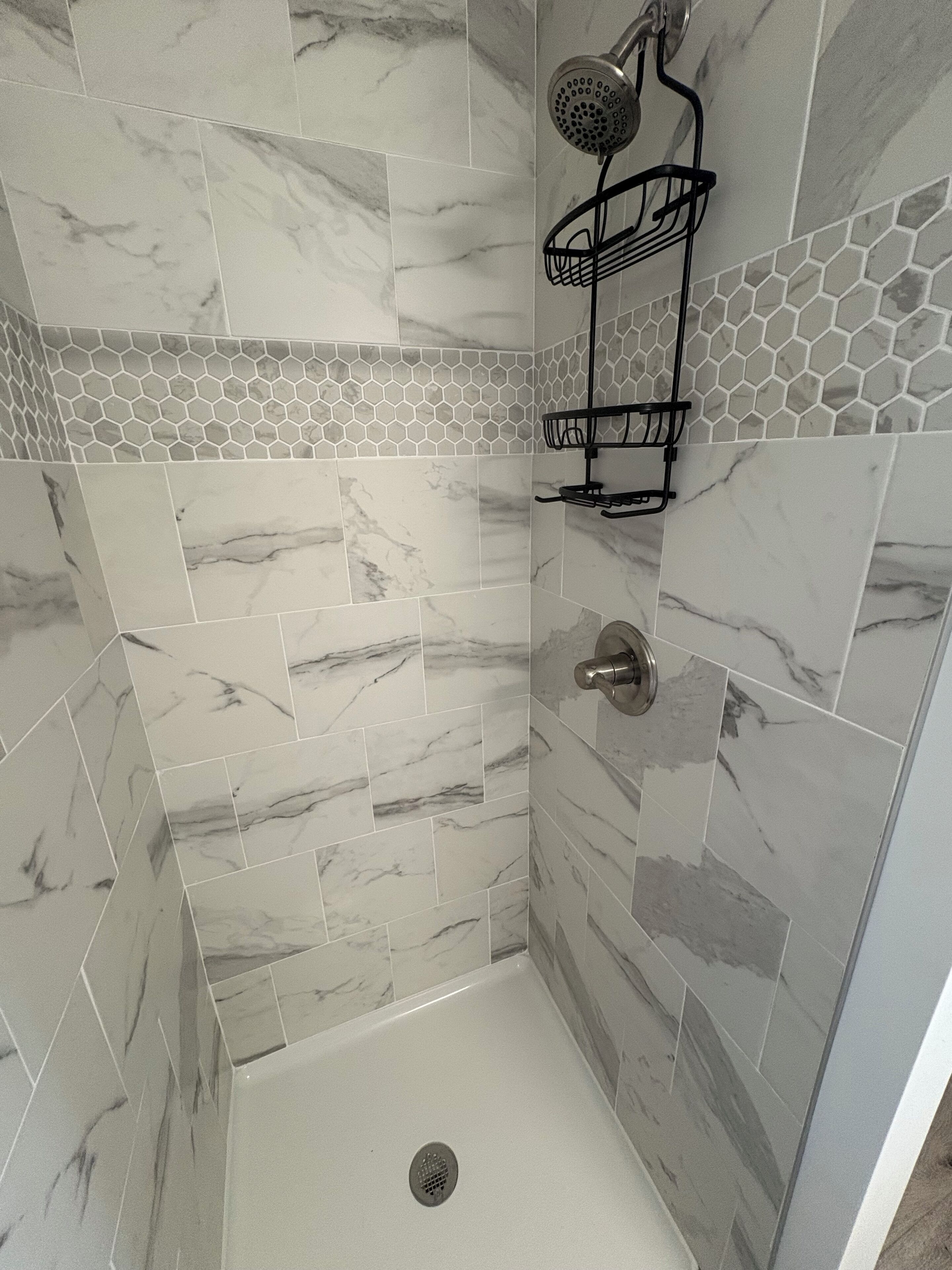 Área de chuveiro com azulejos de mármore, chuveiro e um porta-toalhas preto.