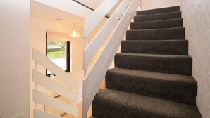 A staircase with carpeted steps and white handrails, leading to a room with a window and a light fixture. - Heronlea Cottage -  Picturesque Scottish setting, 4 guests, pet friendly,  (Dunoon)