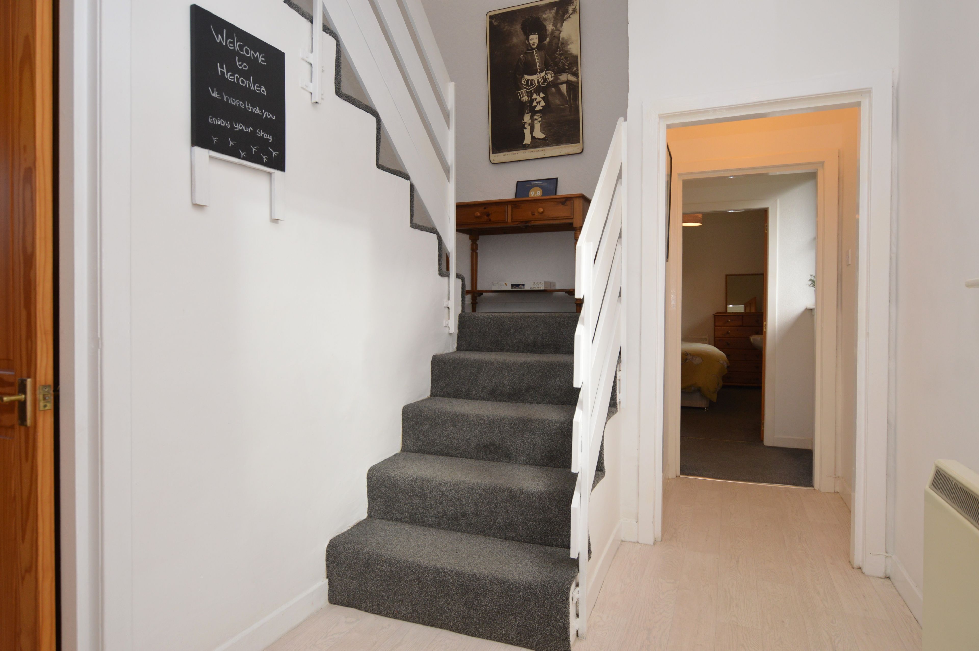 Una escalera con un cartel de bienvenida, un cuadro enmarcado y un banco de madera.