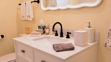 A bathroom with a white marble sink, black faucet, and a mirror above. There are toiletries on the counter and a towel hanging on the wall.