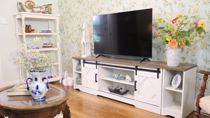 A living room with a TV, white cabinet, and a vase with flowers. - Barby Haus (Bellville)