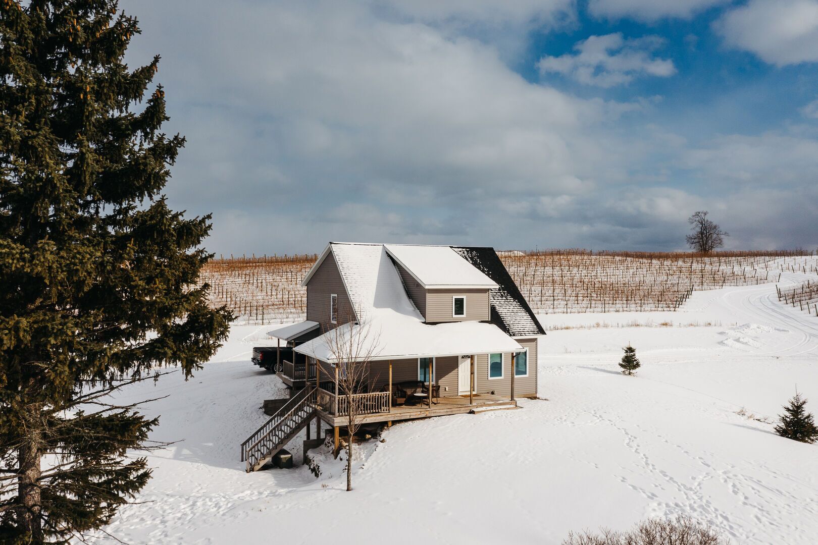 A two-story house with a snow-covered roof, a deck, and a staircase leading to a porch.