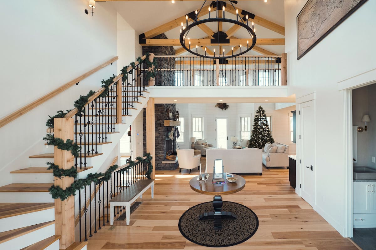 A spacious interior with a wooden staircase, a chandelier, a Christmas tree, and a cozy seating area.