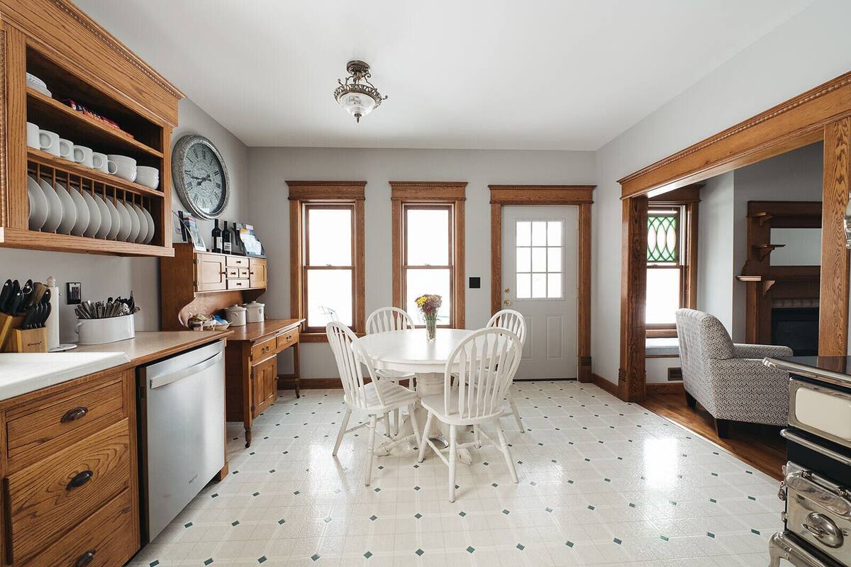 A kitchen with a dining table, white chairs, wooden cabinets, and a clock on the wall.