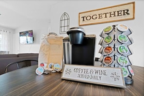 En kaffebar med vin, skilt med 'Kaffe og vin serveres dagligt', kaffemaskine, beholder til kaffekapsler, og et skilt der siger 'SAMMEN'.
