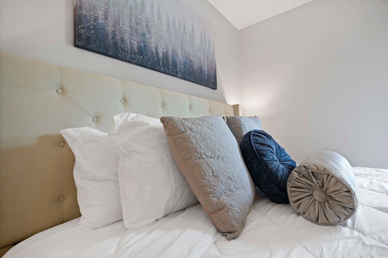 A bed with a tufted headboard, white and patterned pillows, and a large abstract painting above.