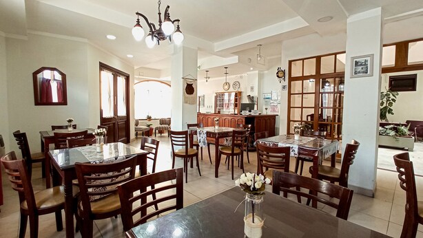 Un comedor espacioso con varias mesas y sillas, una cocina al fondo y un ventanal que proporciona luz natural.