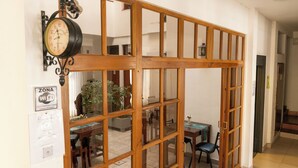 Una habitación con un separador de madera, un reloj en la pared, una mesa con sillas y un cartel que indica acceso a Wi-Fi.