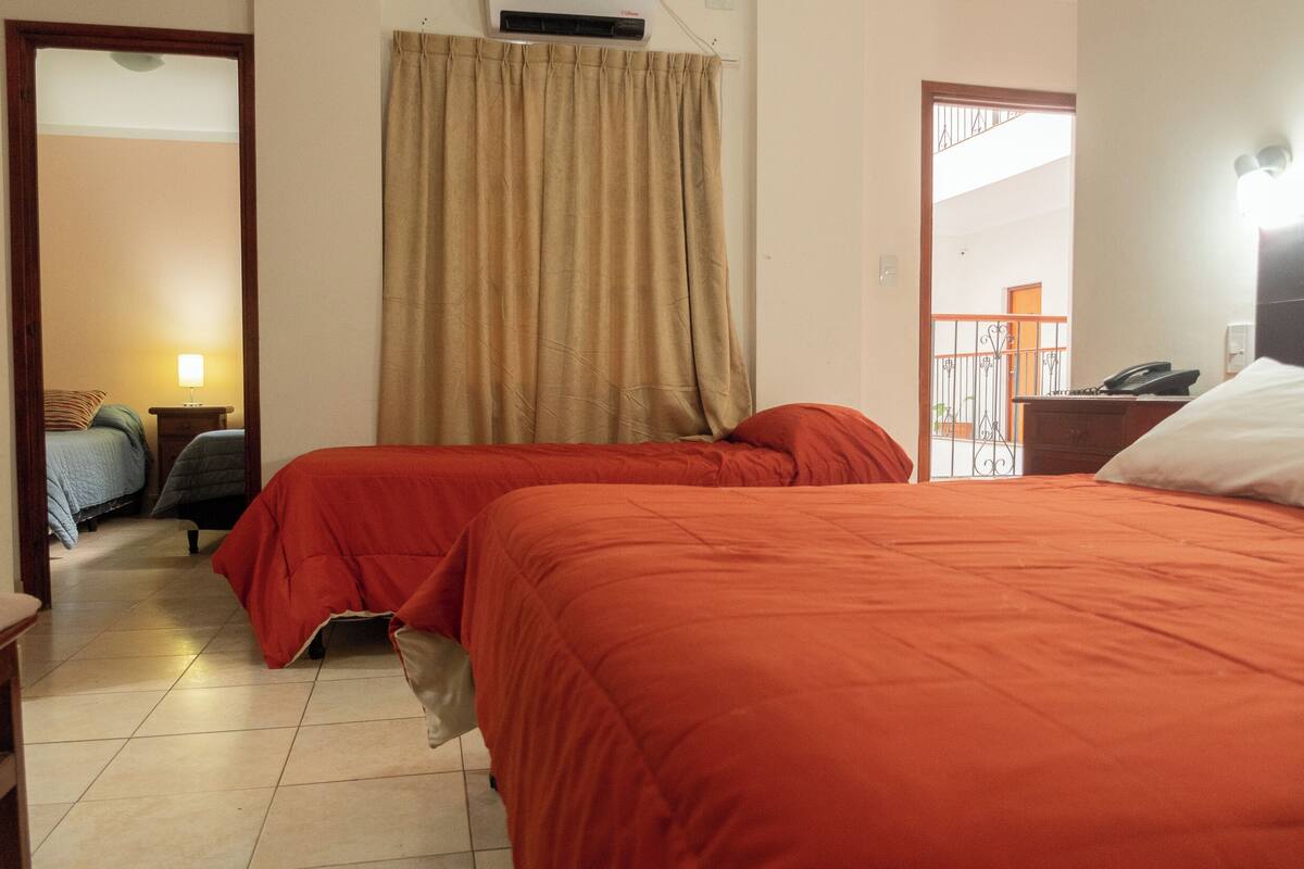 Une chambre d’hôtel avec deux lits, une fenêtre avec des rideaux, une table de chevet avec une lampe et un téléphone sur une petite table à côté du lit.
