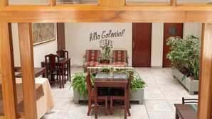Un comedor con una mesa dispuesta para dos personas, rodeada de sillas de madera y un sofá. Un letrero arriba dice "Alto Colonial".