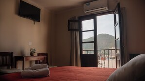 Habitación de hotel con cama, escritorio con silla, televisor montado en la pared y equipo de aire acondicionado.