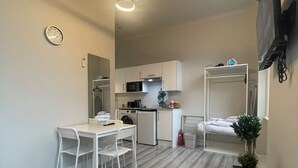Una cocina moderna con armarios blancos, un microondas y una cafetera. Cuenta con un comedor con mesa y sillas blancas.
