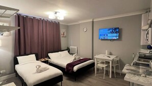 Habitación de hotel con dos camas, un escritorio, un televisor y un kitchenette.