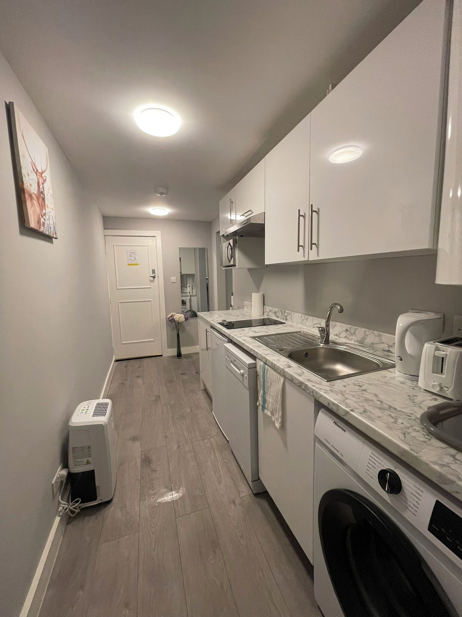 A compact kitchen with white cabinets, a built-in dishwasher, a washing machine, and a marble countertop.