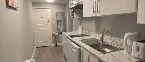 A compact kitchen with white cabinets, a built-in dishwasher, a washing machine, and a marble countertop.