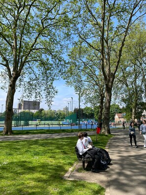 A park with a bench, trees, and a sports field in the background. - Westminster Inn (London)