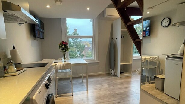 Una cocina moderna con lavadora, una mesa de comedor con sillas, una escalera y un reloj en la pared.