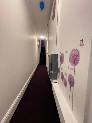 A hallway with a purple carpet, white walls, and a door at the end. - Westminster Inn (London)