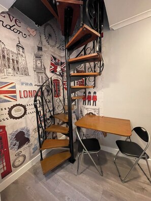 A corner room with a spiral staircase, a wooden desk, two chairs, and a wall decorated with London-themed illustrations. - Westminster Inn (London)