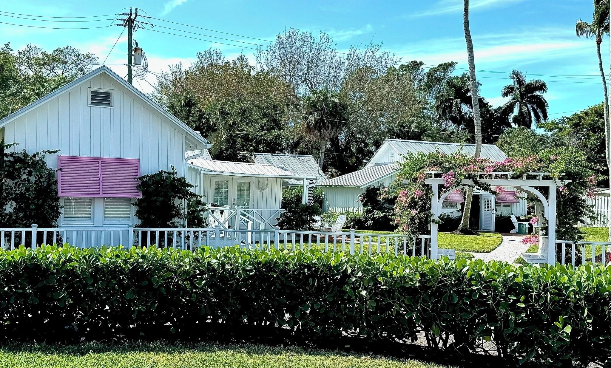 A white house with a porch, surrounded by greenery and a white fence.