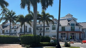 A residential street with palm trees, a paved driveway, and a two-story house with a balcony.