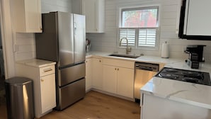 A modern kitchen with a stainless steel refrigerator, a dishwasher, a stove, and a window with blinds.
