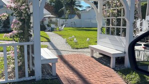 A white pergola with a brick pathway leading to a bench.