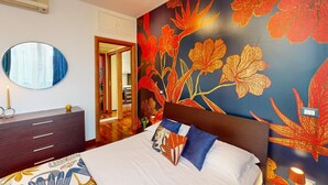 A bedroom with a large bed, a dresser, a mirror, and a vibrant floral wall mural.