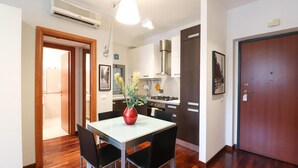 A modern kitchen with a dining area, wooden flooring, and a red vase on the table.