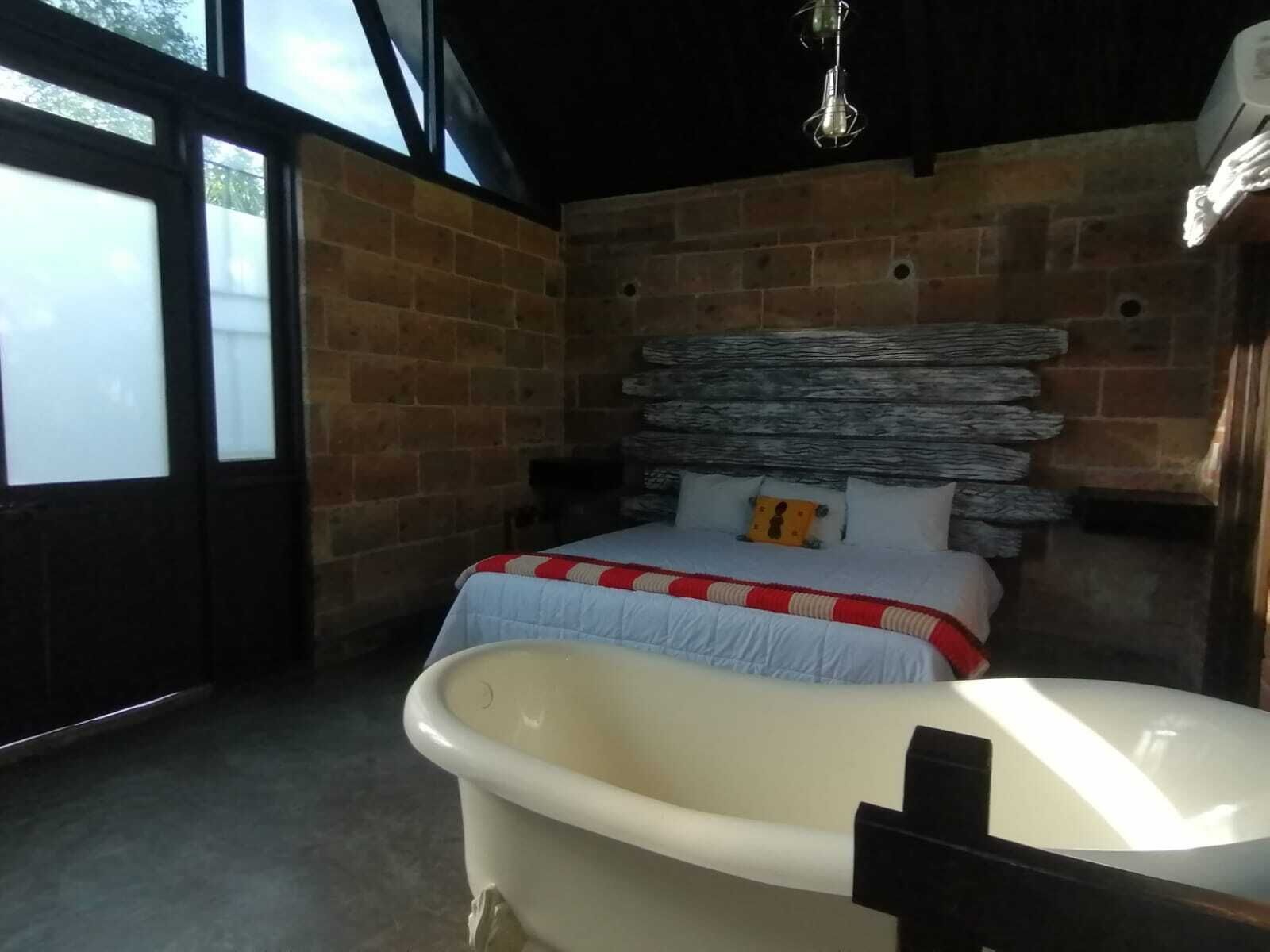 A room with a brick wall, a bed with a red and white striped bedspread, and a white bathtub.