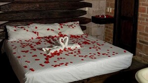 A bed with rose petals and a heart-shaped towel, a brick wall, and a wooden headboard. - Las Chalatas (El Fuerte)
