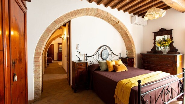 A bedroom with a bed, wooden wardrobe, arched doorway, and a mirror with flowers.