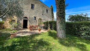 A stone building with a garden patio, outdoor seating, and a large tree.