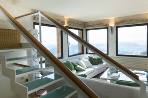 A modern interior with a staircase, a white sofa with green cushions, and large windows offering a city view. - Zafferano Rooftop Terrace Tower House (San Gimignano)