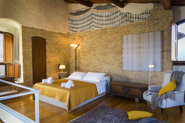A cozy room with a bed, a chair, a lamp, and a wooden chest. - Zafferano Rooftop Terrace Tower House (San Gimignano)