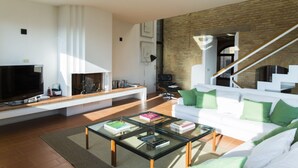 A modern living room with a flat-screen TV, a glass coffee table, a white sofa with green cushions, and a brick wall. - Zafferano Rooftop Terrace Tower House (San Gimignano)
