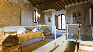A cozy room with a bed, a wooden table, a suitcase, and a bookshelf. - Zafferano Rooftop Terrace Tower House (San Gimignano)