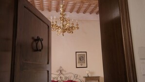 Un dormitorio con puerta de madera, cama con ropa de cama roja, candelabro y un cuadro enmarcado en la pared.
