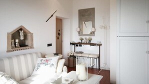 A living room with a striped sofa, a small table with a candle, a mirror, and a shelf with decorative items. - Zaffiro Bianco Central home (San Gimignano)
