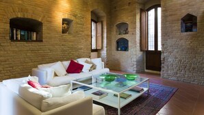 Un salon spacieux avec un canapé blanc, une table basse en verre surmontée de bols verts et un mur en briques.
