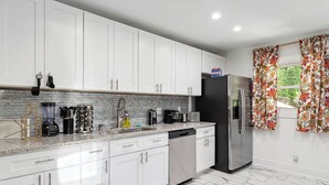 Una cocina moderna con armarios blancos, un refrigerador de acero inoxidable y una encimera con diversos electrodomésticos.