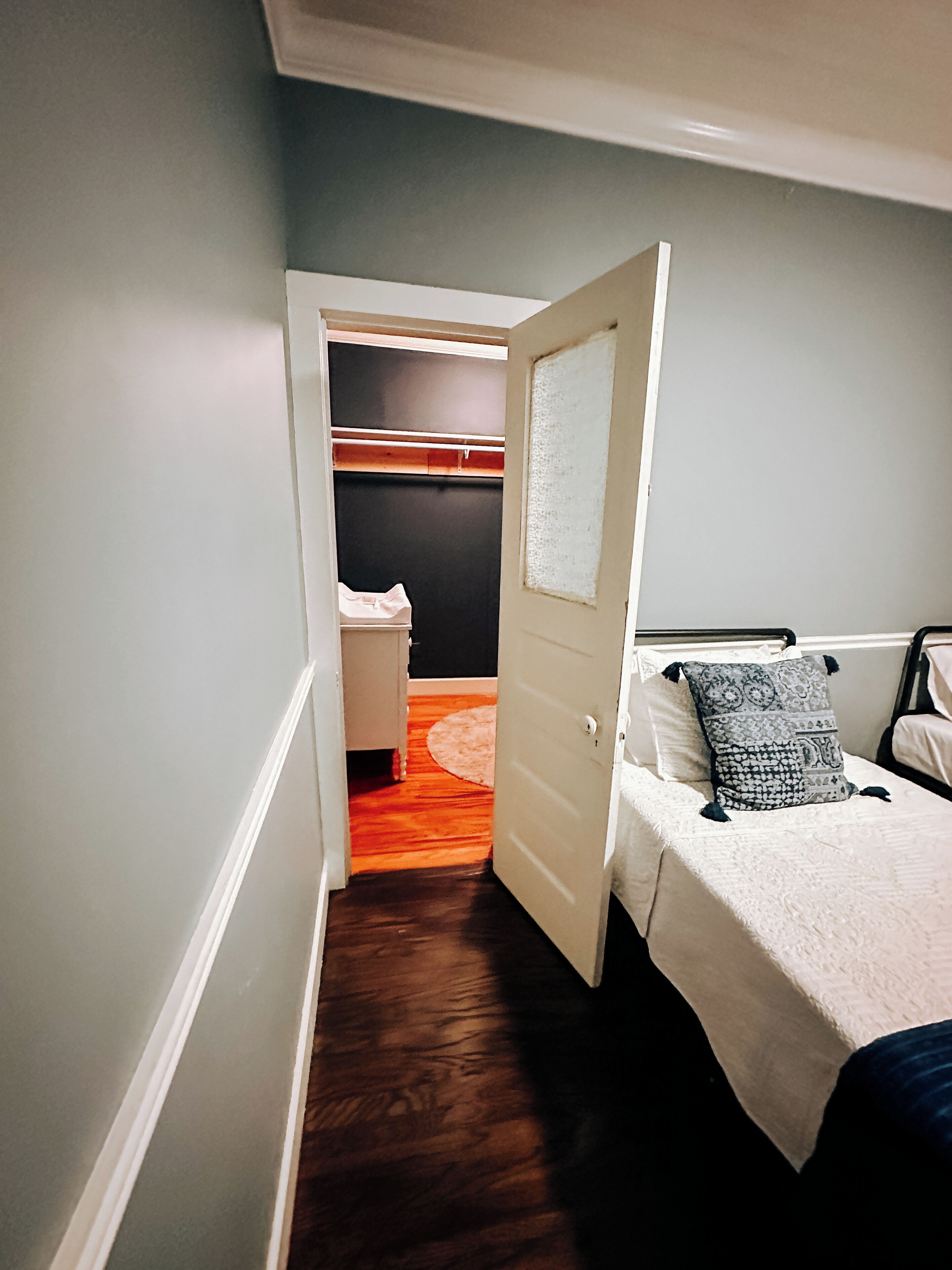 Corredor estreito que dá acesso a um quarto com cama, mesa de cabeceira e guarda-roupa.