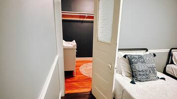 Corredor estreito que dá acesso a um quarto com cama, mesa de cabeceira e guarda-roupa.