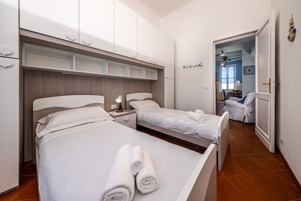 Une chambre d’hôtel avec deux lits, une armoire, une table de chevet et une salle de bain visible à travers une porte ouverte.