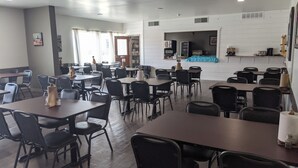 Ein geräumiger Essbereich mit mehreren Tischen und Stühlen, ein Küchenbereich im Hintergrund und ein sauberes, modernes Interieur.