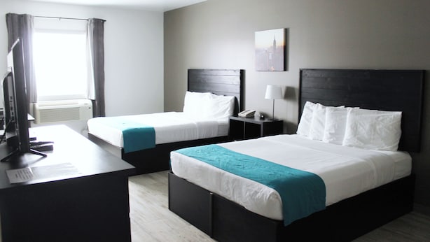 Ein Hotelzimmer mit zwei Betten, einem Schreibtisch, einem Stuhl, einem Fernseher und einem Fenster mit Vorhängen.