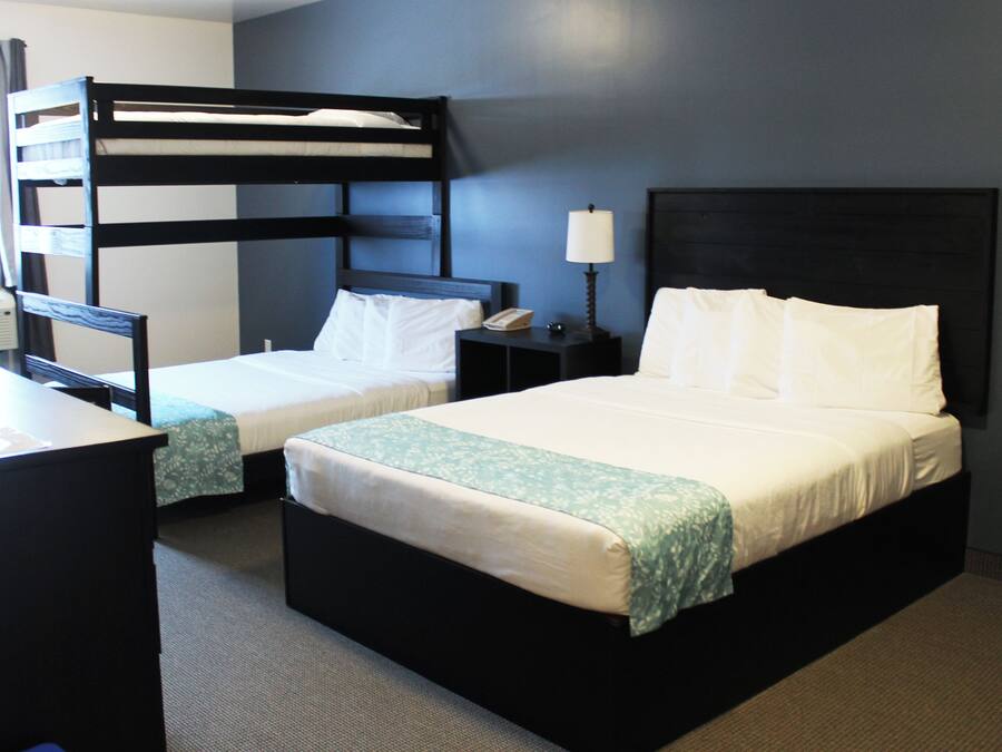 A hotel room with two beds, a bunk bed, a desk, a nightstand, and a lamp.