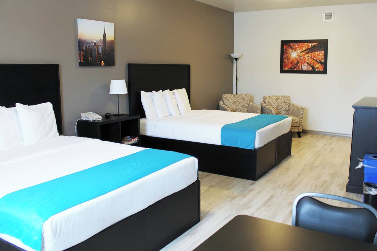 Ein Hotelzimmer mit zwei Betten, einem Schreibtisch, einem Stuhl und Bildern an den Wänden.