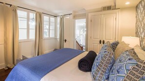 A bedroom with a large bed, a wardrobe, and a door leading to another room. - Charming 2BR in Historic Savannah! (Savannah)