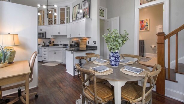 A modern kitchen with white cabinets, a central island, and a dining area with wooden chairs and a vase of flowers. - Charming 2BR in Historic Savannah! (Savannah)